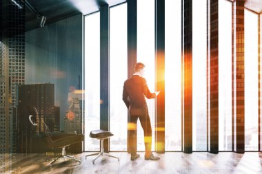 Adam koyu ahşap duvarlar, ahşap zemin ve pencerenin yanında kahverengi koltuk ayakta minimalist tavan oturma odasında. Çift tonlu görüntü pozlaması