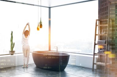 Kadın gri duvarlar, panoramik banyo köşesinde döşeli kat, beyaz küvet, havlu ve beyaz çekmeceli ahşap raflara. Çift tonlu görüntü pozlaması