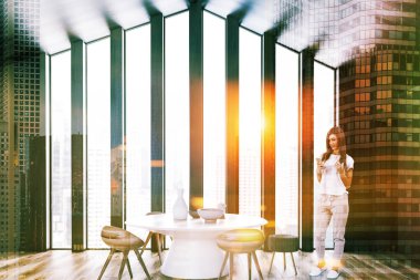 İç tavan yemek odası ile gri ve koyu ahşap duvarlar, ahşap zemin ve yuvarlak beyaz masası ahşap ve gri sandalye ile bir kadın. Çift tonlu görüntü pozlaması