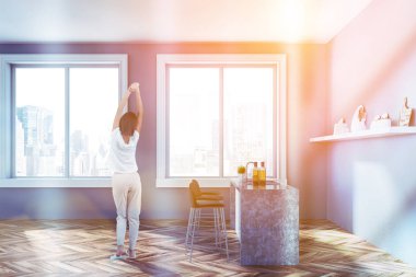 Minimalist mutfak Gri duvarlar, ahşap zemin, pencere eşiği ile cityscape, gri ve beyaz bar tabureleri ile ve kaplar ile raf ile duran kadın. Tonlu görüntü