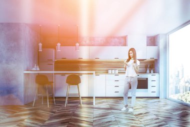 Kadın şık mutfak iç beton duvarlar, ahşap zemin, panoramik penceresi, beyaz mutfak tezgahı ve dolapları ve gri tabureleri olan çubuk. Tonlu görüntü
