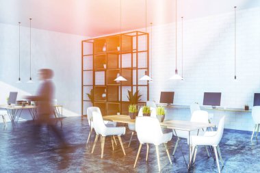 Adam beyaz ve tuğla duvarlar, uzun bilgisayar tablo ayakta duvarın yanında, daha küçük ahşap masa bilgisayarlarla ve tablo ortasındaki beyaz sandalye ile office köşesinde. Görüntü bulanık tonda