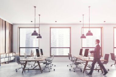 Beyaz ve açık ahşap duvar, çatı windows, beton zemin ve hafif ahşap bilgisayar tabloları satırları açık alan ofiste yürüyüş iş adamı. Tonlu görüntü