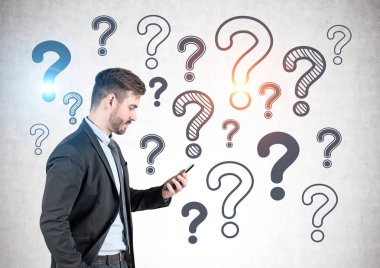 Yan görünümü koyu takım elbise ve bakarak onun smartphone ayakta beton duvarının yakınında birçok soru işareti üzerinde çizilmiş olan sakallı genç işadamı portresi