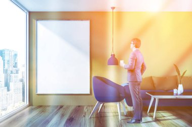 Çatı katında salon sarı duvarlar, ahşap zemin, mavi ve bej kanepe ve siyah sehpa ve dikey poster duvara yakın mavi koltuk ile iç adam. Resim sahte tonda