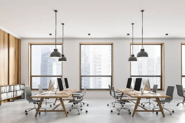 Side view of open space office with white and light wooden walls, loft windows, concrete floor and rows of light wooden computer tables. 3d rendering