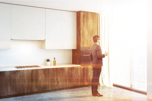 男は白い壁 コンクリートの床 木のカウンター トップ ホワイトの食器棚とキッチンの窓を見るします トーンのイメージ — ストック写真