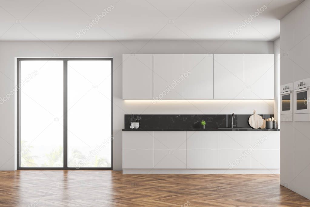 Interior of modern kitchen with white walls, wooden floor, white cupboards, countertops with built in sink and two ovens in the wall. 3d rendering
