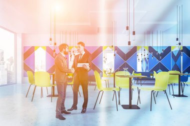 İki iş adamları iç panoramik Kafe'nin mavi duvar, beton zemin, mavi kanepeler ve Sehpalar yakınındaki koltuklar ve kare tablolar yakınındaki sarı sandalyeler ile konuş. Tonlu görüntü