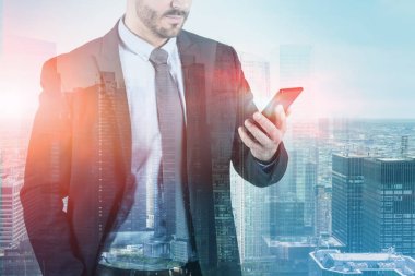 Tanınmayan portresi, onun smartphone ayakta cityscape arka plan üzerinde seyir işadamı sakallı. İletişim iş kavramı. Çift tonlu görüntü pozlaması