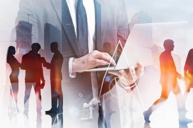 Dizüstü bilgisayar ve iş ekibi üyeleri önlerinde grafik ile modern cityscape arka plan üzerinde duran tanınmayan işadamı. Tonlu görüntü çift pozlama