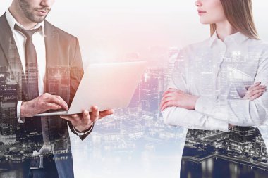 Tanınmayan işadamı laptop ve kendine güvenen işkadını ile ayakta kullanarak silah gece cityscape arka plan üzerinde geçti. Yönetim kavramı. Çift tonlu görüntü pozlaması