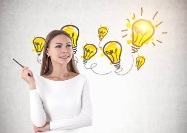 Beyaz giyen ve birçok Işık Ampüller beton duvarla yakınındaki bir kalem ayakta tutan sarı saçlar ile gülümseyen genç kadın.