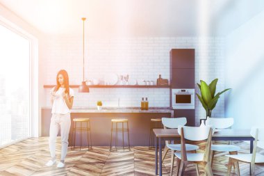 Kadın iç mutfak beyaz tuğla duvarlar, ahşap zemin, panoramik penceresi, gri ve mermer mutfak tezgahı ve bar tabureleri ile. Ahşap masa sandalye ile. Tonlu görüntü