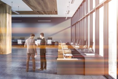 Businessmen in interior of modern office with gray and wooden walls, tiled floor, and rows of gray and wooden computer tables standing along the wall and the window. Toned image