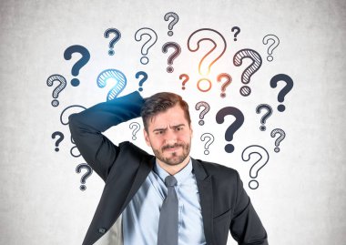 Portrait of confused thinking bearded businessman scratching his head standing near concrete wall with many question marks drawn on it. Concept of solution search