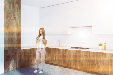 Kadın beyaz duvarlar, beton zemin, ahşap mutfak tezgahı ve beyaz dolapları modern mutfak köşesinde. Tonlu görüntü