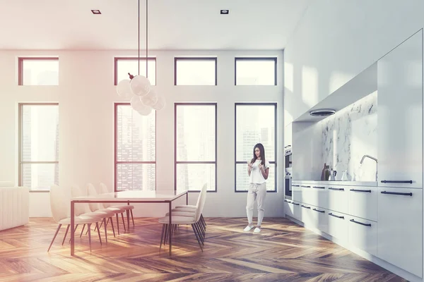 现代厨房的侧面景观 有白色和白色的大理石墙 木地板 带两个炉灶的白色台面和带椅子的白色桌子 女人与智能手机 色调图像 — 图库照片