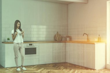 Kadın beyaz duvarlar, ahşap zemin ve yerleşik fırın ve lavabo beyaz mutfak tezgahı ile küçük mutfak köşesinde. Çift tonlu görüntü pozlaması