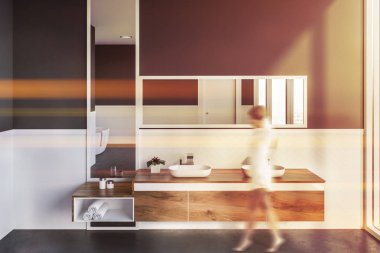 Modern banyo beyaz ve gri duvarlar, beton zemin, çift lavabo üstündeki dikey ve yatay ayna ile ahşap tezgah üzerinde duran iç kadında. Görüntü bulanık tonda