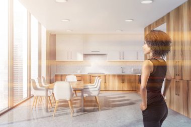 Kadın iç beyaz ve beton duvarlar, beton zemin, ahşap mutfak tezgahı, modern mutfak dolapları ve uzun bir masa sandalye ile beyaz. Tonlu görüntü