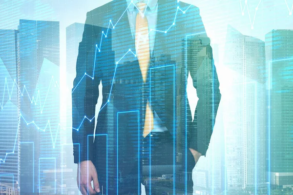 Portrait of unrecognizable businessman in dark suit and yellow tie standing with hand in pocket in city with double exposure of graph. Toned image. Stock market concept