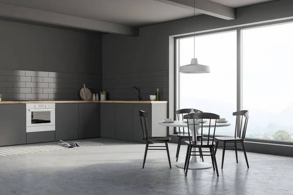 Corner of modern kitchen with gray walls, concrete floor, large window, gray countertops and round white table with black chairs. 3d rendering