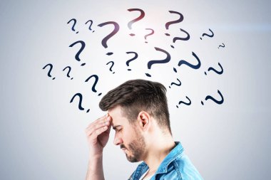 Soru işareti üzerinde çizilmiş olan kot gömlek ve sahip güçlü baş ağrısı ayakta beyaz duvarının yakınında giyen sakallı genç adam yan görünüm. Zor sorun kavramı