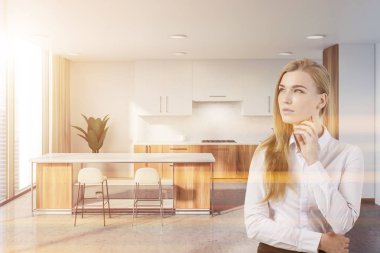 İç beyaz duvarlar, beton zemin, beyaz dolapları ve ahşap mutfak tezgahı ile şık mutfak ve dışkı ile beyaz çubuğu kadında. Tonlu görüntü