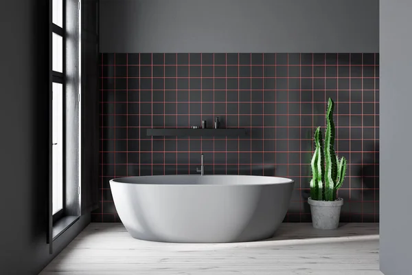 Interior of minimalistic bathroom with gray and black tile walls, concrete floor, gray bathtub standing near window and black shelf with creams. 3d rendering
