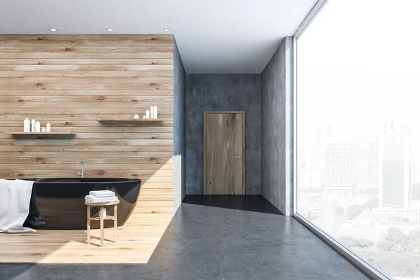 室内的全景浴室与混凝土和木墙 水泥地板 黑色浴缸与白色毛巾 并与洗发水和面霜上面的货架 — 图库照片