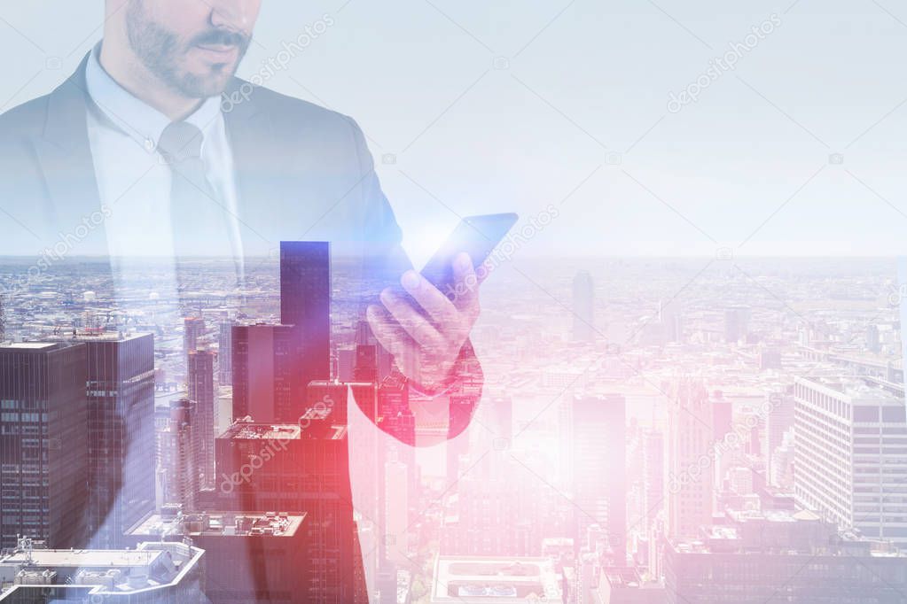 Side view of unrecognizable young businessman with beard looking at his smartphone standing in modern city. Toned image double exposure