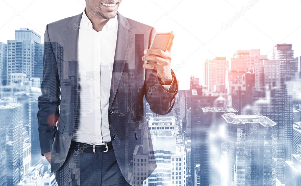 Cheerful unrecognizable African American businessman looking at his smartphone standing in modern city. Toned image double exposure