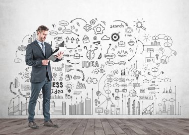 Pano tutarak ve bu iş stratejisi kroki üzerine beton duvarla yakın duran bakarak koyu takım elbise sakallı genç işadamı portresi.