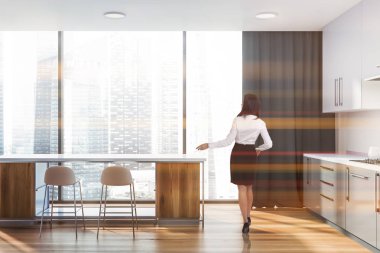 Kadın iç beyaz duvarlar, ahşap zemin, gri mutfak tezgahı ve dolapları ile panoramik mutfak ve beyaz ve ahşap bar tabureleri ile. Tonlu görüntü