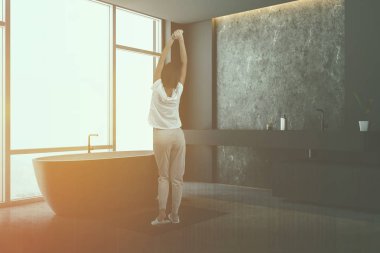 Kadın gri ve beton duvarlar, büyük pencere, beton zemin, şık banyo köşesinde beyaz havlu uzun gri lavabo ve küvet. Çift tonlu görüntü pozlaması