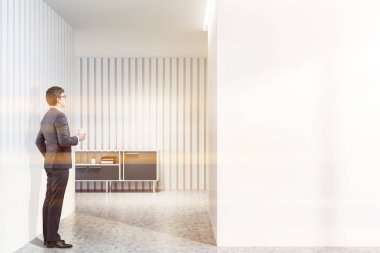 Adam beyaz salon iç beyaz duvarlar, beton zemin ve gri klasörler ve Kırtasiye ile kabine ile ayakta. Duvar kadar alay et. Tonlu görüntü