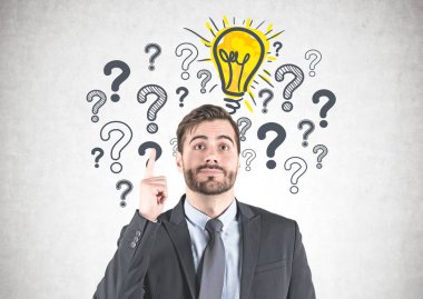 Gülümseyen genç iş adamı yukarı seyir ve parmak ayakta yakınındaki soru işaretleri ve ampul üzerinde çizilmiş olan beton duvar ile işaret eden sakallı koyu takım elbise.