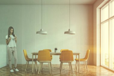 Beyaz duvarları, ahşap zemin, geniş pencere ve sarı sandalye ile uzun ahşap masa ile minimalist yemek odası iç kadında. Çift tonlu görüntü pozlaması