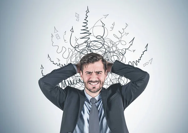 Portrait of stressed young businessman in suit standing with clenched teeth and painful expression near gray wall with arrows drawn around his head. Concept of stress