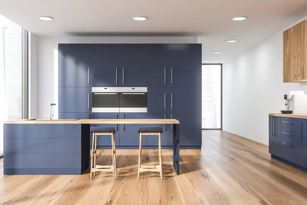 Interior of modern kitchen with white walls, wooden floor, blue cupboard with two built in ovens and blue and wooden bar with stools and sink. 3d rendering