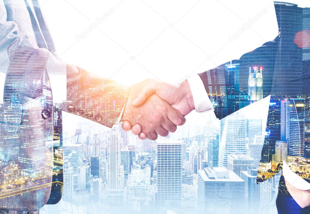 Close up of two unrecognizable businessmen shaking hands over modern cityscape background. Concept of partnership. Toned image double exposure