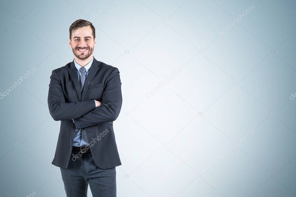 Smiling businessman with crossed arms, gray wall