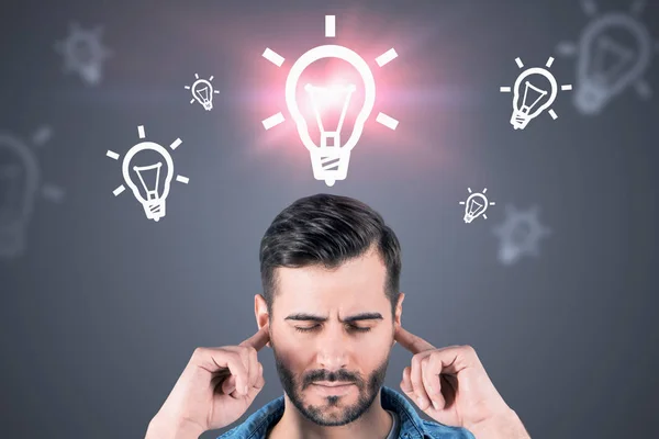 Stressed man covering ears, light bulbs on gray