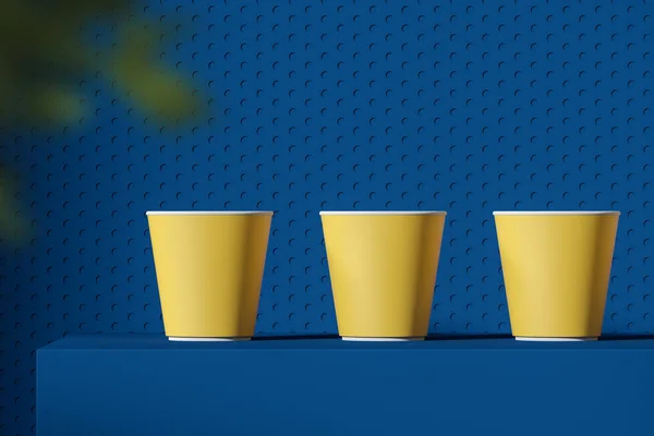 Drie gele papieren bekers staande op blauwe tafel — Stockfoto