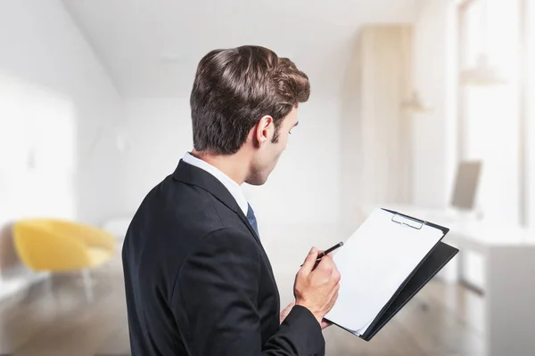 Young businessman with clipboard in blurry office — Stock Photo, Image