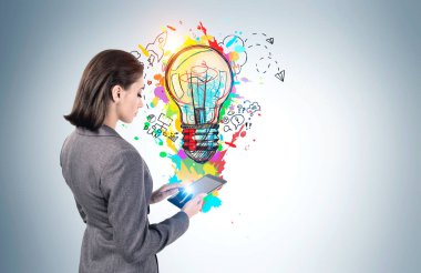 Ciddi Avrupalı genç iş kadınının gri duvarın yanındaki tabletini renkli bir iş fikri eskiziyle birlikte kullanışının yan görüntüsü. Yaratıcılık ve teknoloji kavramı. Model