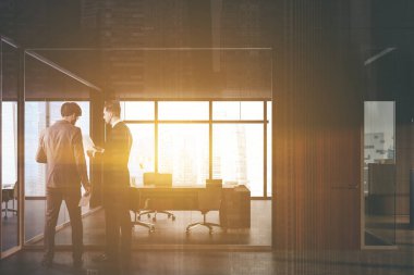 Gri ve camdan duvarları, tahta kapısı ve ziyaretçiler için sandalyeleri olan bilgisayar masası olan modern CEO ofisinin yakınında konuşan iki yönetici. Danışmanlık kavramı. Renkli resim çift pozlama