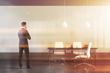 Minimalist CEO ofisinde beyaz ve gri duvarları ve ziyaretçiler için sandalyeleri olan orijinal masası olan kendinden emin genç iş adamının arka görüntüsü. Liderlik kavramı. Tonu ayarlanmış resim