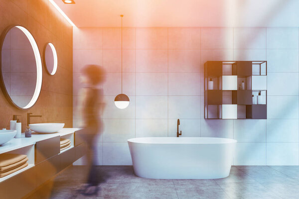 Blurry young African American woman standing in luxury bathroom with white and brown walls, double sink with round mirrors and comfortable bathtub. Toned image